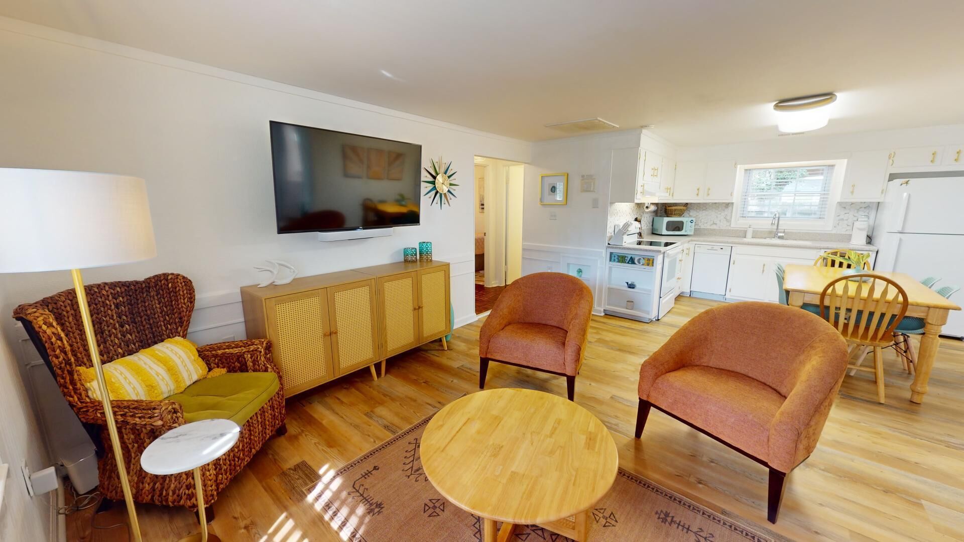 A compact living space with a sofa, armchairs, a coffee table, a TV, a kitchen area, and a dining table.