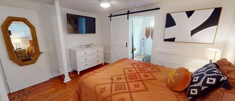 Un dormitorio con una cama grande, un aparador, un espejo, un ventilador de techo y una puerta corredera.