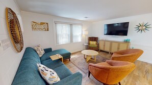 A modern living room with a sofa, armchairs, a coffee table, and a TV. - Nobody's Tybee Shack by Tybee Vacation Rentals (Tybee Island)