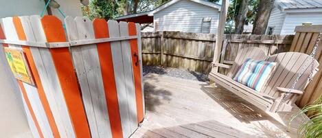 A wooden deck leading to a fenced backyard with a swing chair and a small shed.