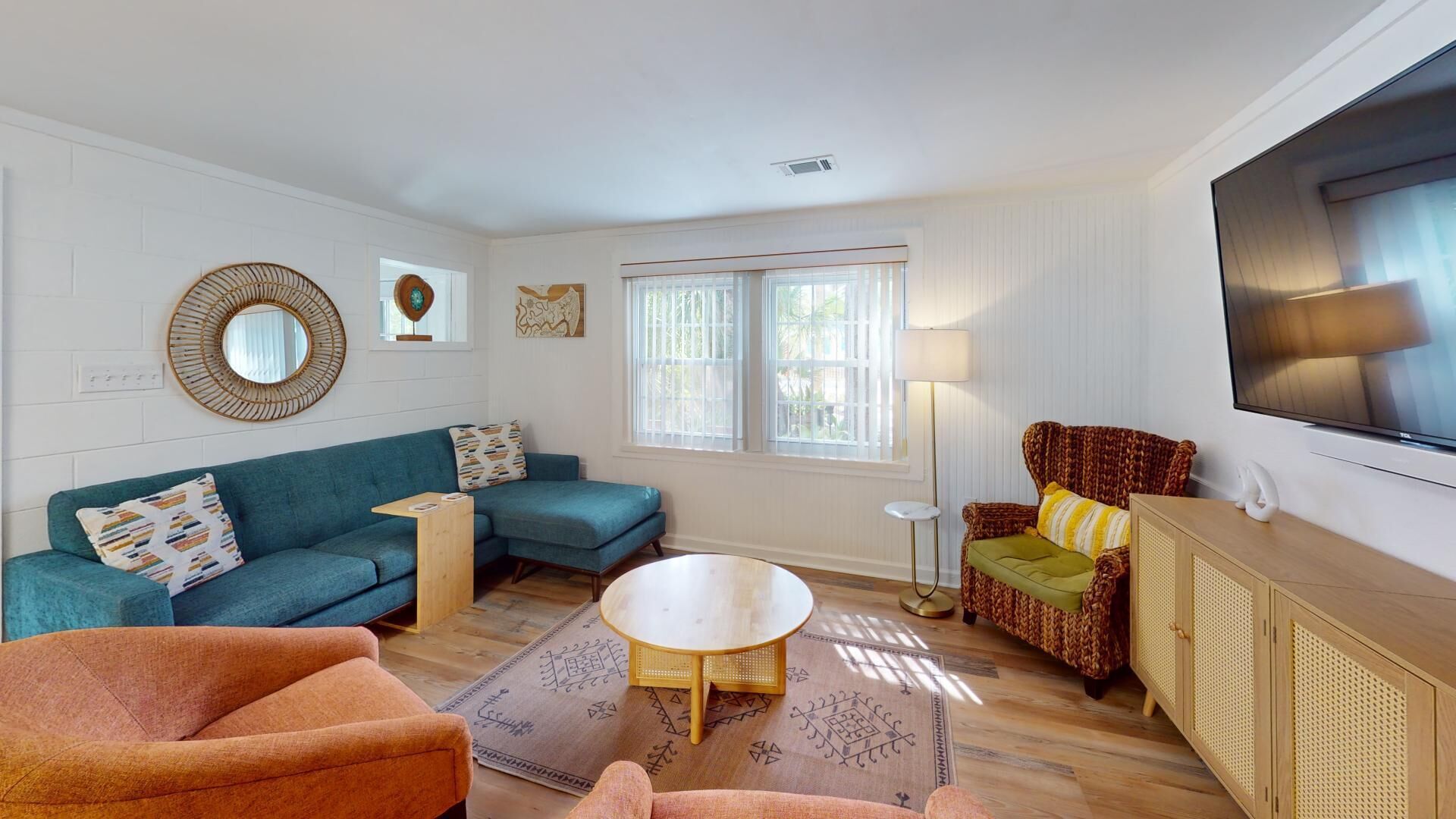 A living room with a teal sofa, a brown armchair, a round coffee table, and a TV mounted on the wall.
