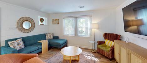 A living room with a teal sofa, a brown armchair, a round coffee table, and a TV mounted on the wall.
