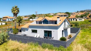 Una casa moderna de dos pisos amb teulada inclinada, un balcó i una zona de pati pavimentada.