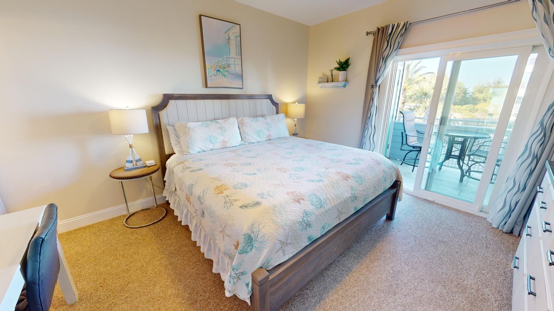 A bedroom with a bed, bedside tables, a lamp, a painting on the wall, and a view of the outside through a sliding door.