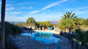Une piscine entourée d’une terrasse en bois, bordée de palmiers et agrémentée de chaises, d’où l’on peut admirer l’océan et, au loin, un cargo.