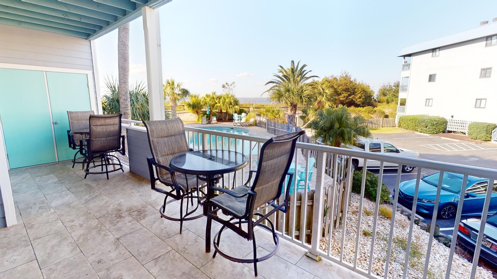 A balcony with a pool table, chairs, and a view of a parking area and buildings.