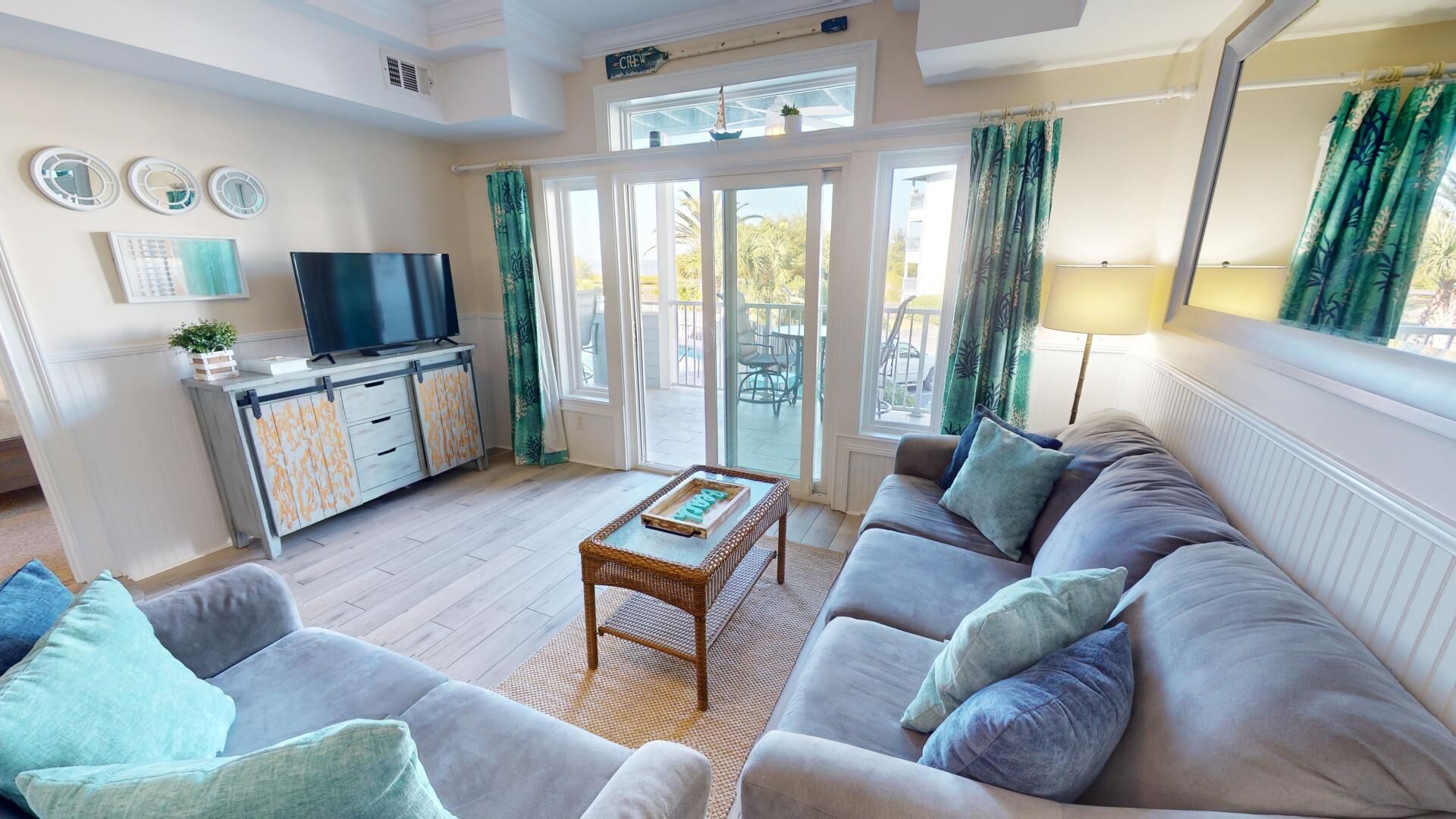 A living room with a sofa, a coffee table, a TV, and a balcony with curtains.