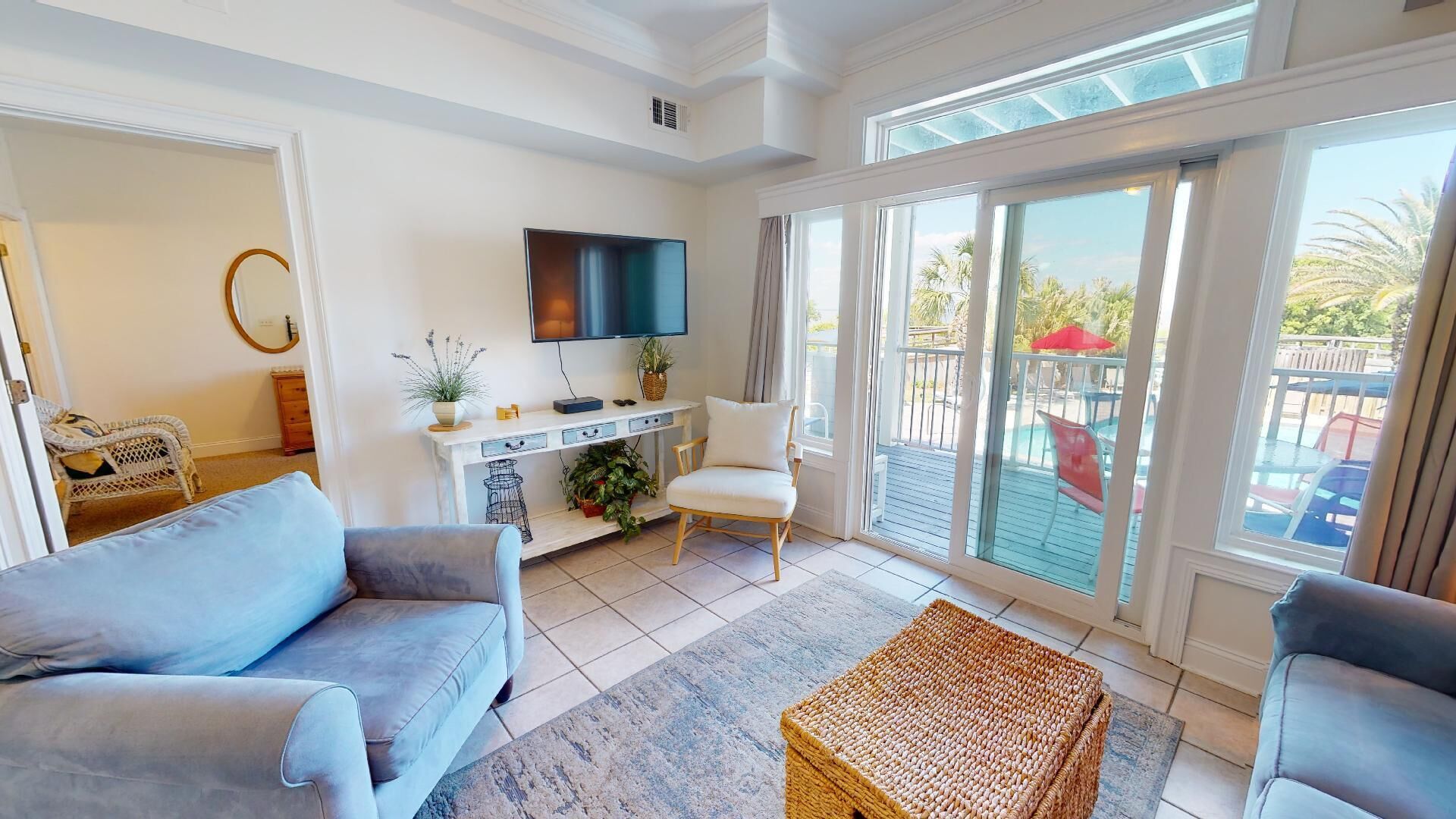A living room with a sofa, a chair, a TV, a console table with plants, and a view of the outside balcony.