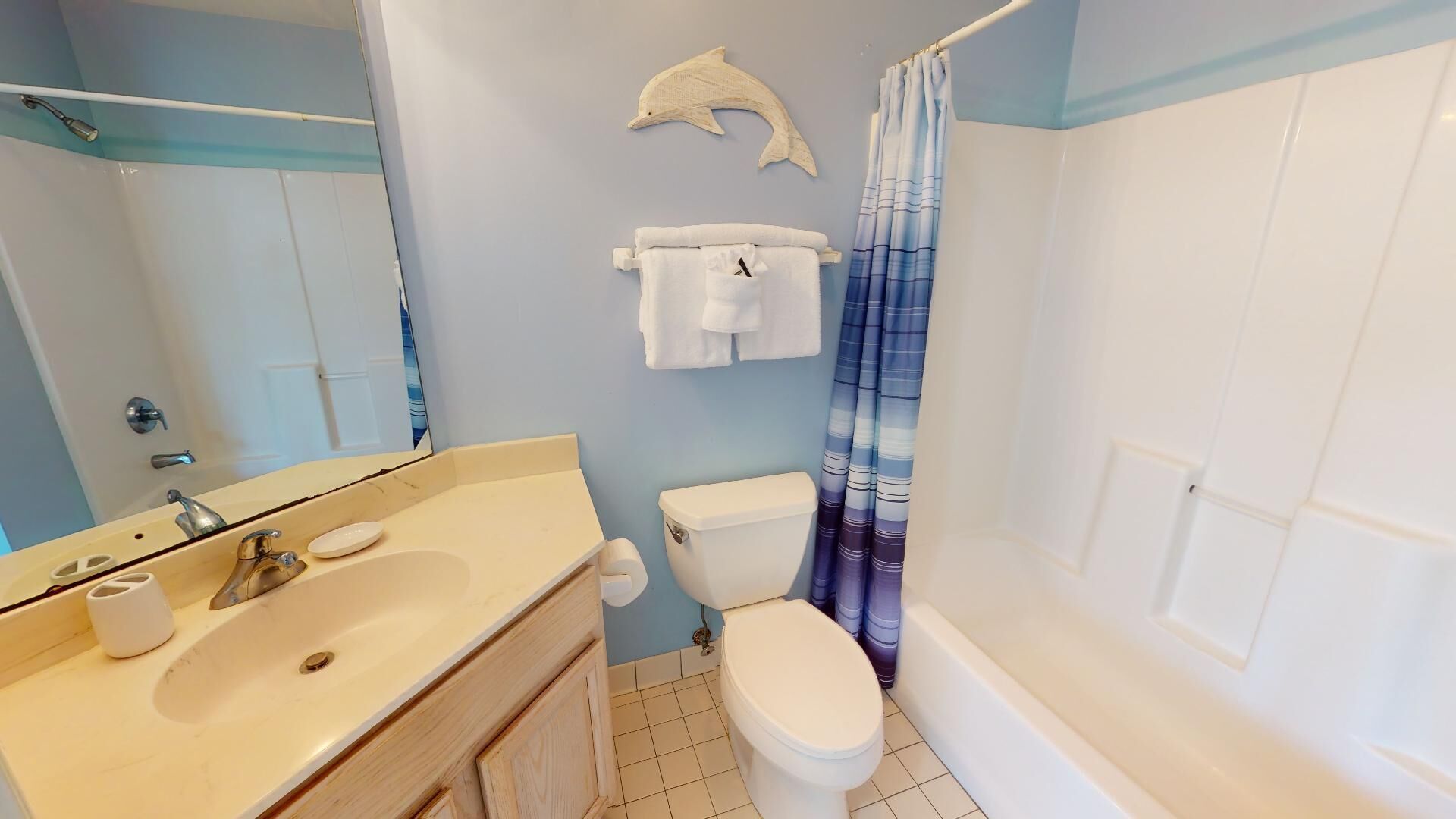 A bathroom with a bathtub, toilet, sink, and a dolphin-shaped towel rack.
