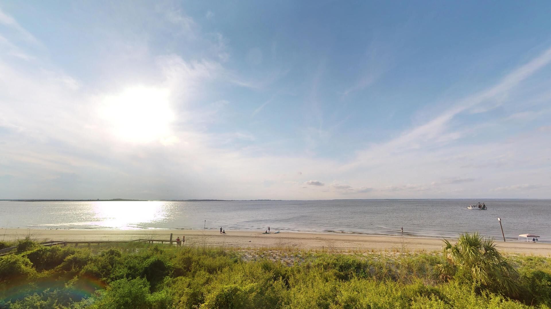 En strand med en træpromenade, en fjern båd og en klar himmel.