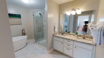 Un baño moderno con ducha envuelta en vidrio, una bañera independiente y un lavamanos con un espejo grande y tres luces.