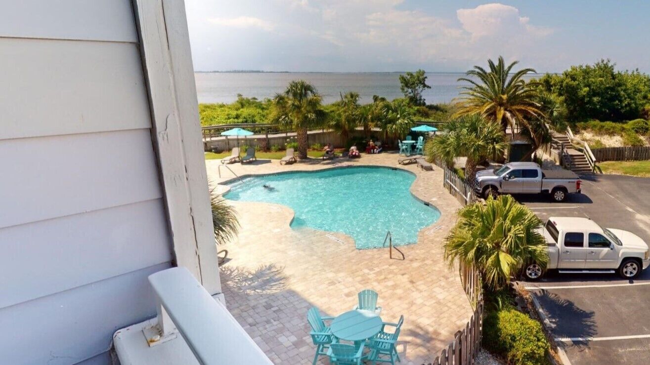 A swimming pool with a view of the ocean, surrounded by palm trees and outdoor seating.
