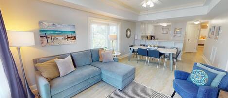 A modern living room with a sofa, a dining area, and a kitchen in the background.