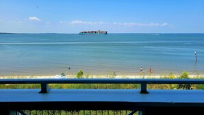 A view of a calm sea with a cargo ship in the distance, a sandy beach, and a few people walking along the shore. - Bay View Villas 3 by Tybee Vacation Rentals (Tybee Island)