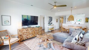 A modern living room with a flat-screen TV, wooden coffee table, and a dining area with a round table and chairs. - Bay View Villas 3 by Tybee Vacation Rentals (Tybee Island)