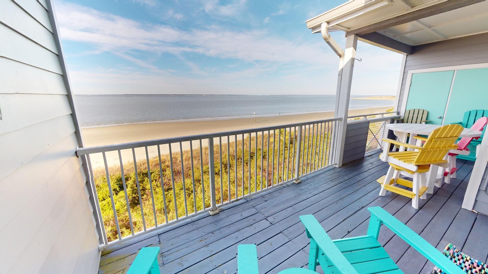 A wooden deck with a view of the beach, outdoor seating, and a covered area with a table and chairs.