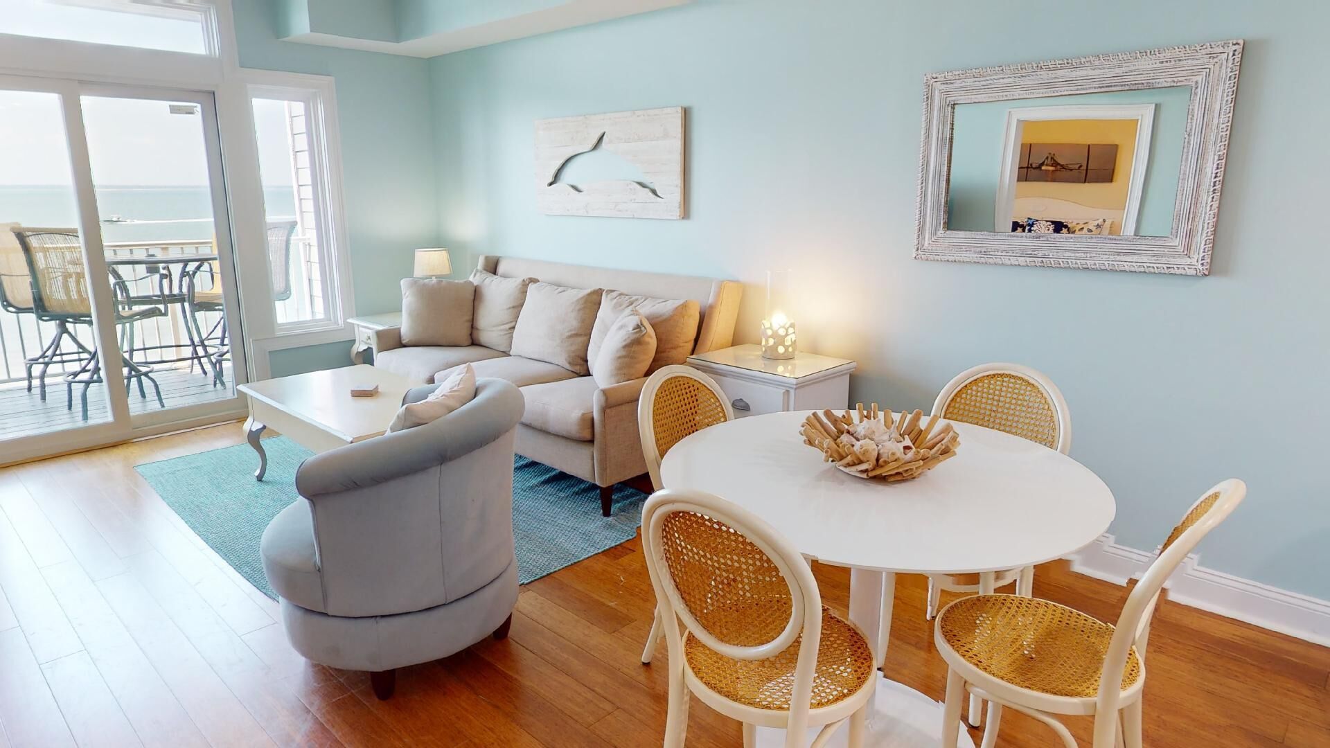 A living room with a sofa, a round table with chairs, a lamp, and a wall-mounted mirror.