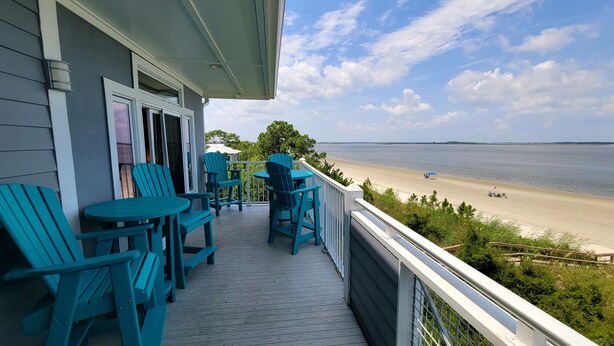 A wooden deck with blue Adirondack chairs and a table, overlooking a beach. - Bay View Villas 3 by Tybee Vacation Rentals (Tybee Island)