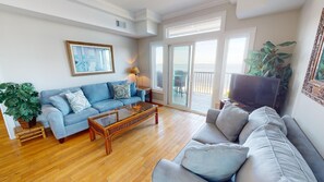 A living room with a blue sofa, a wooden coffee table, a television, and a balcony with a view. - Bay View Villas 3 by Tybee Vacation Rentals (Tybee Island)