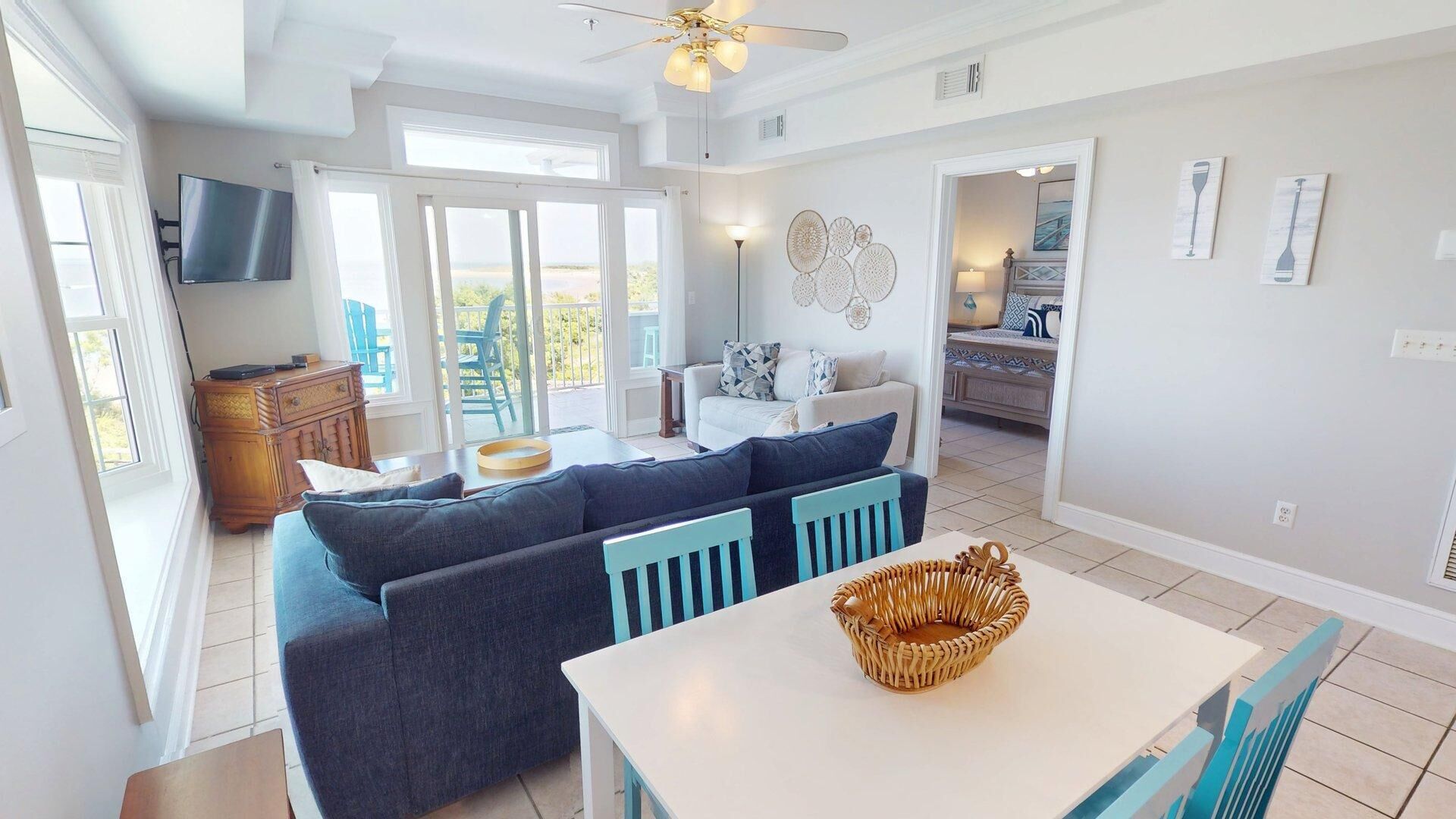 A spacious living room with a large sofa, a dining table, and a ceiling fan.