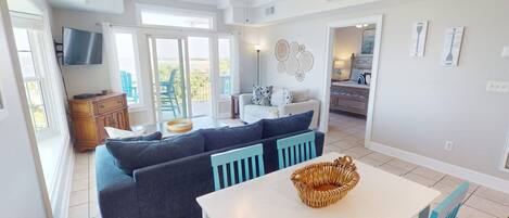 A spacious living room with a large sofa, a dining table, and a ceiling fan.