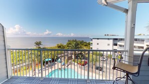 A balcony with a view of a swimming pool, a beach, and a building across the water. - Bay View Villas 3 by Tybee Vacation Rentals (Tybee Island)