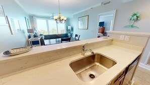Eine moderne Küche mit einer großen Spüle, eine Essecke mit Tisch und Stühlen und ein Wohnzimmer mit Sofa und Fernseher.