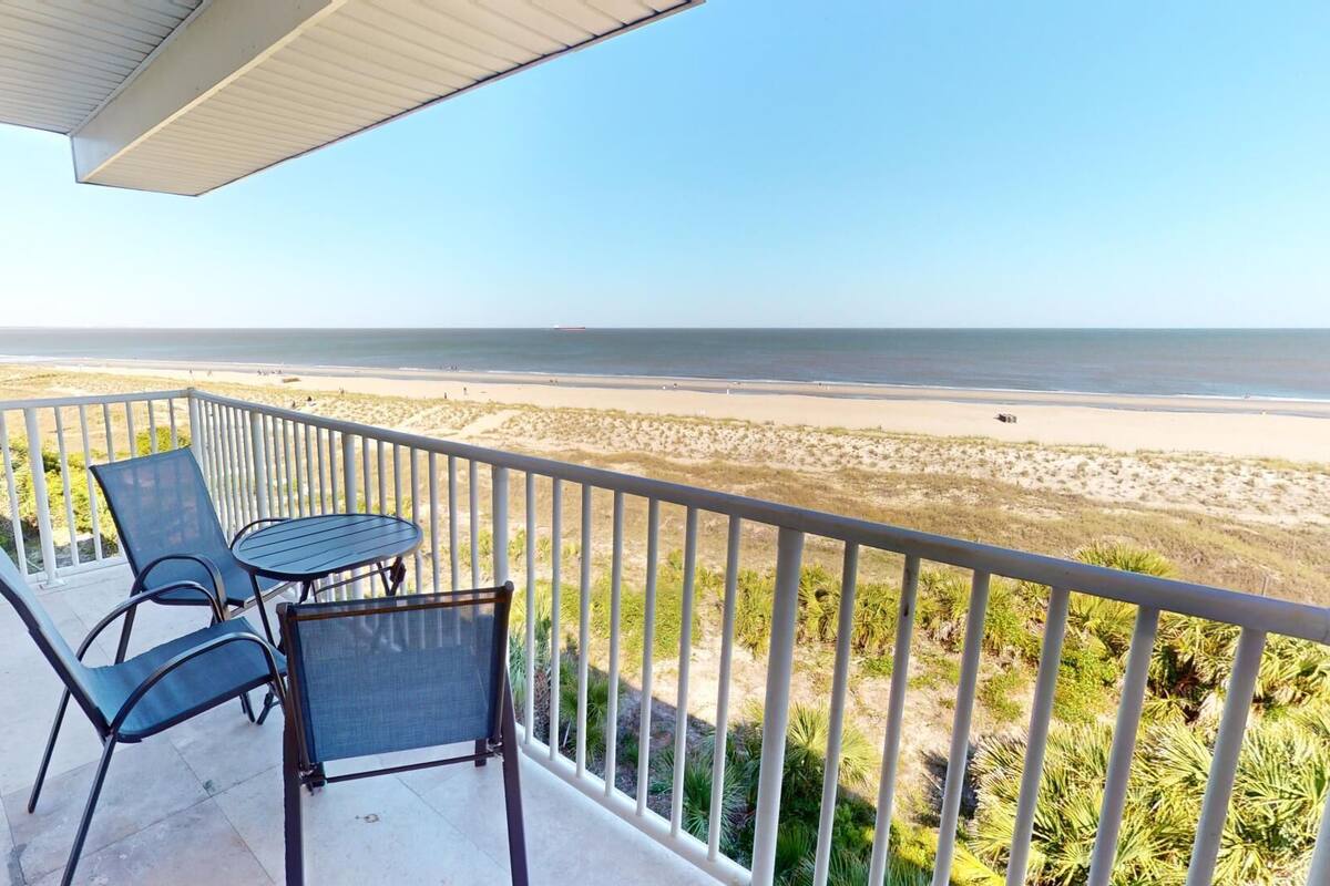 A balcony with a table and chairs overlooking a beach.