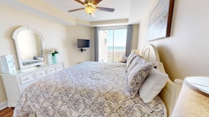 A bedroom with a large bed, a dresser, a mirror, a TV, and a balcony with a view.