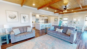 A spacious living area with a large gray sofa, a wooden ceiling, and a kitchen in the background. - Beach Ya To It Tybee Vacation Rentals (Tybee Island)