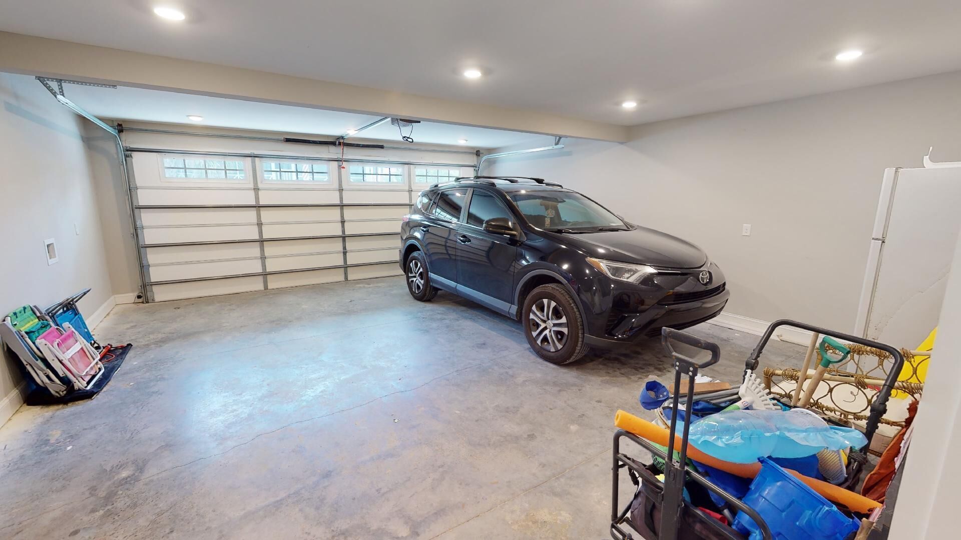 Un garage dans lequel est garé un SUV noir, avec un sol en béton et une porte métallique sur laquelle sont posés divers objets.