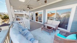 A covered outdoor deck with a sofa, chairs, and a table. - Beach Ya To It Tybee Vacation Rentals (Tybee Island)