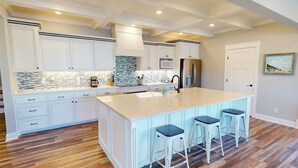 A kitchen with white cabinetry, a large island with bar stools, a microwave, and a refrigerator. - Beach Ya To It Tybee Vacation Rentals (Tybee Island)