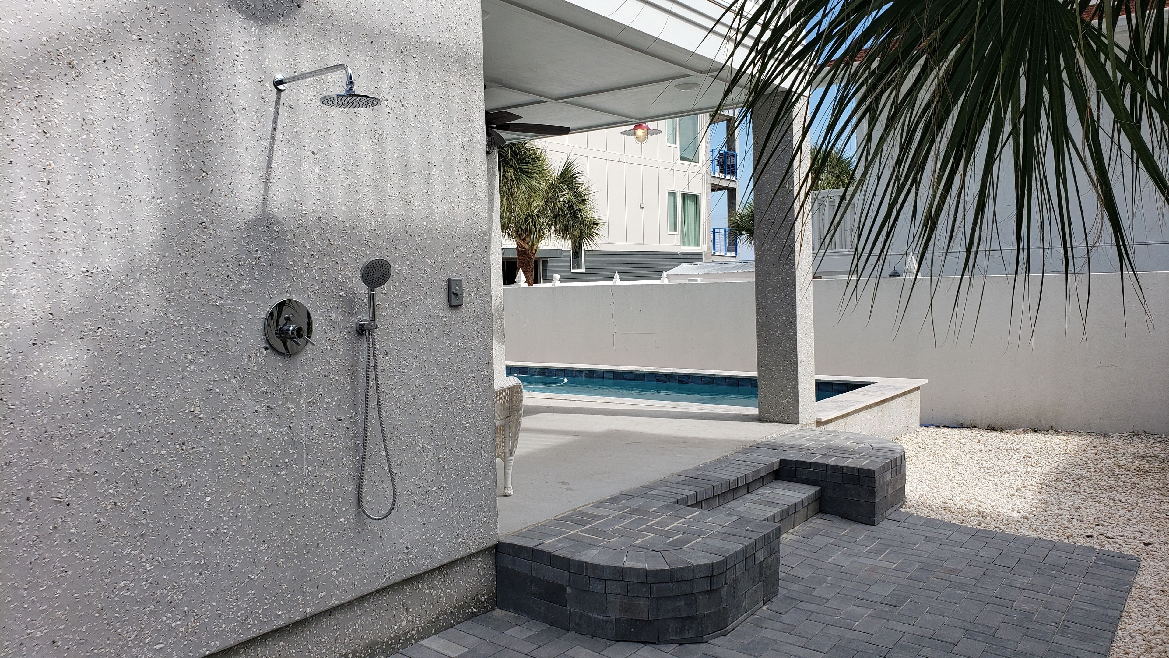 A modern outdoor shower area with a built-in pool, stone steps, and a palm tree.