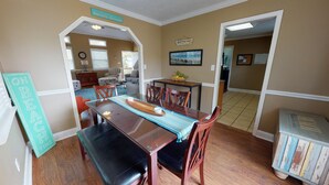 A dining area with a wooden table, benches, and a blue-striped table runner. There are chairs around the table, and a sign on the wall reads "Welcome to our Beach House." - Beachy Keen Tybee Vacation Rentals (Tybee Island)
