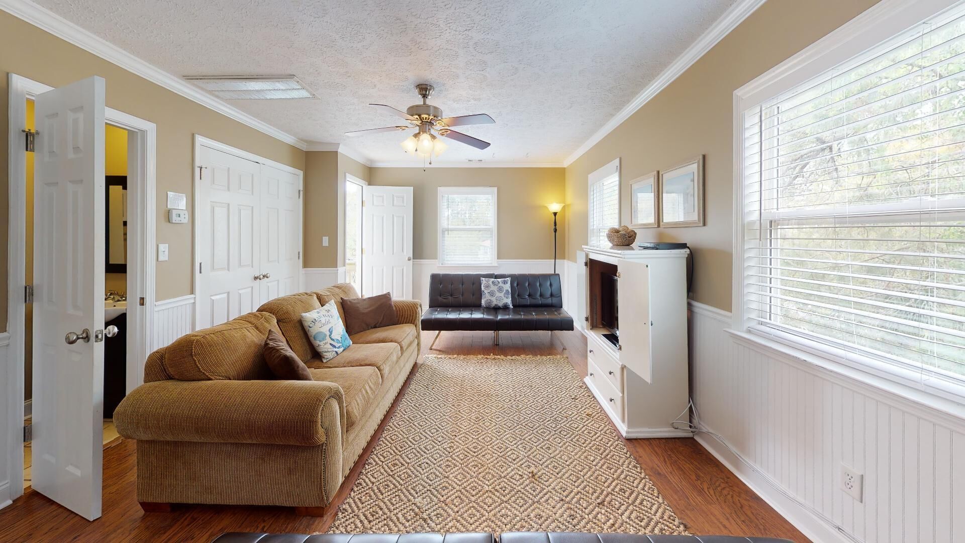 A living room with a brown sofa, a patterned rug, a ceiling fan, and a white cabinet.