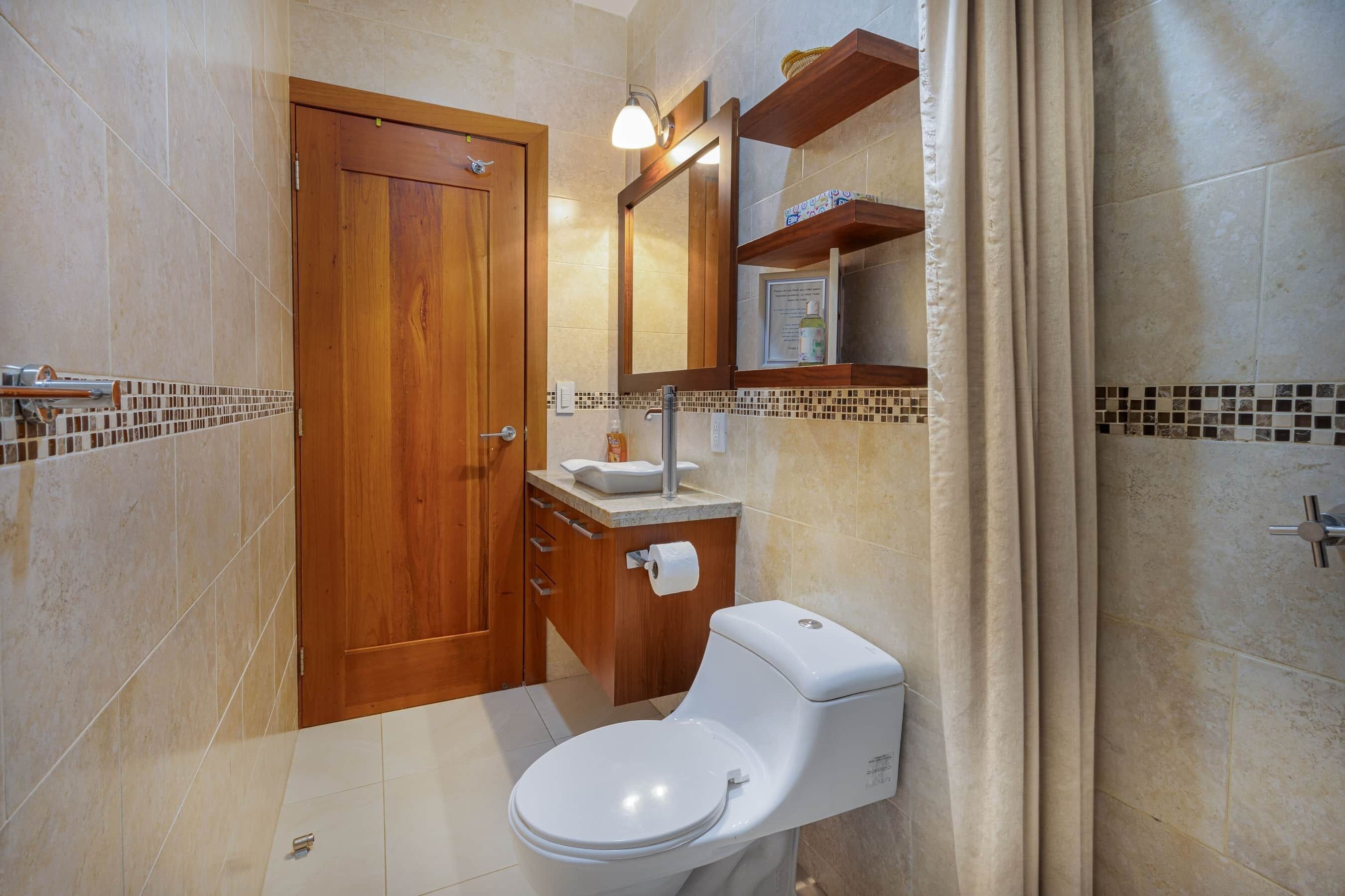 Een badkamer met een houten deur, een wit toilet, een wastafel met een spiegel erboven en een douchegordijn.