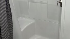 Ducha amb porta de vidre, plat de dutxa i barra per penjar tovalloles.