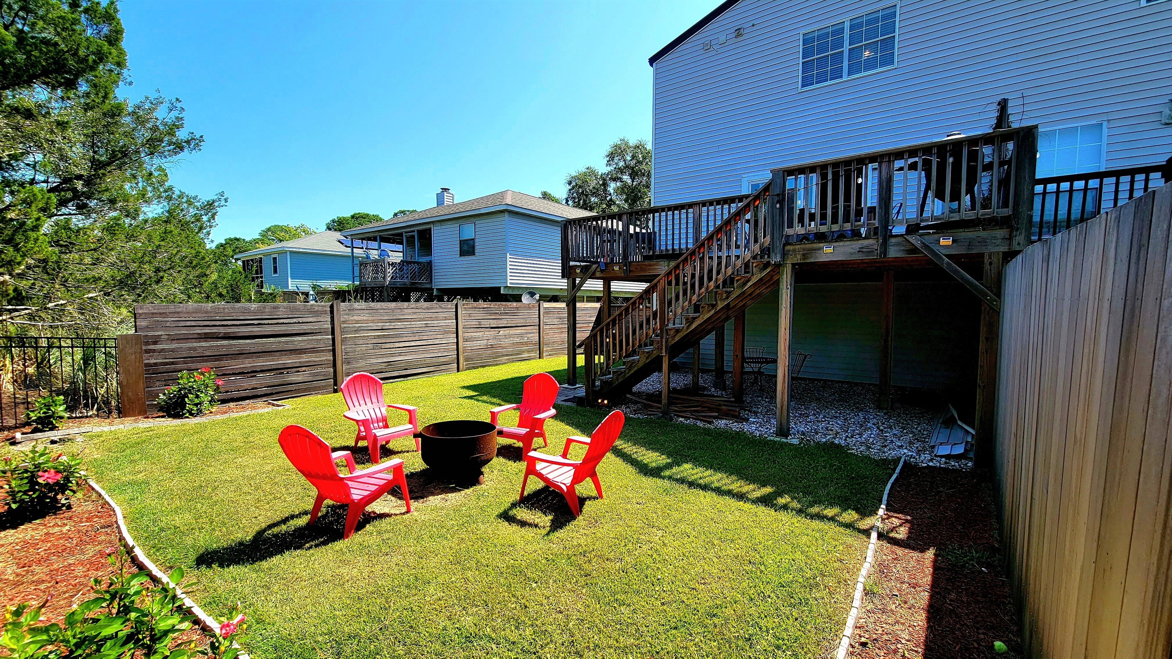 A backyard with a wooden deck, a staircase leading to a second-story deck, and red Adirondack chairs.