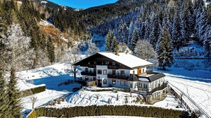 A multi-story chalet with a snow-covered roof, surrounded by a forest and a mountain backdrop. - Hotel Kristall (Kleinarl)