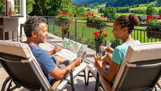 A couple on a balcony with a mountain view, outdoor seating, and potted plants. - Hotel Kristall (Kleinarl)