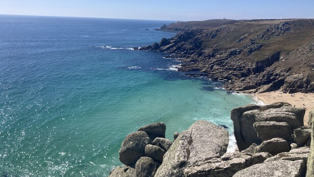 Un paysage côtier caractérisé par des falaises rocheuses, une plage de sable et des eaux d’un bleu limpide.
