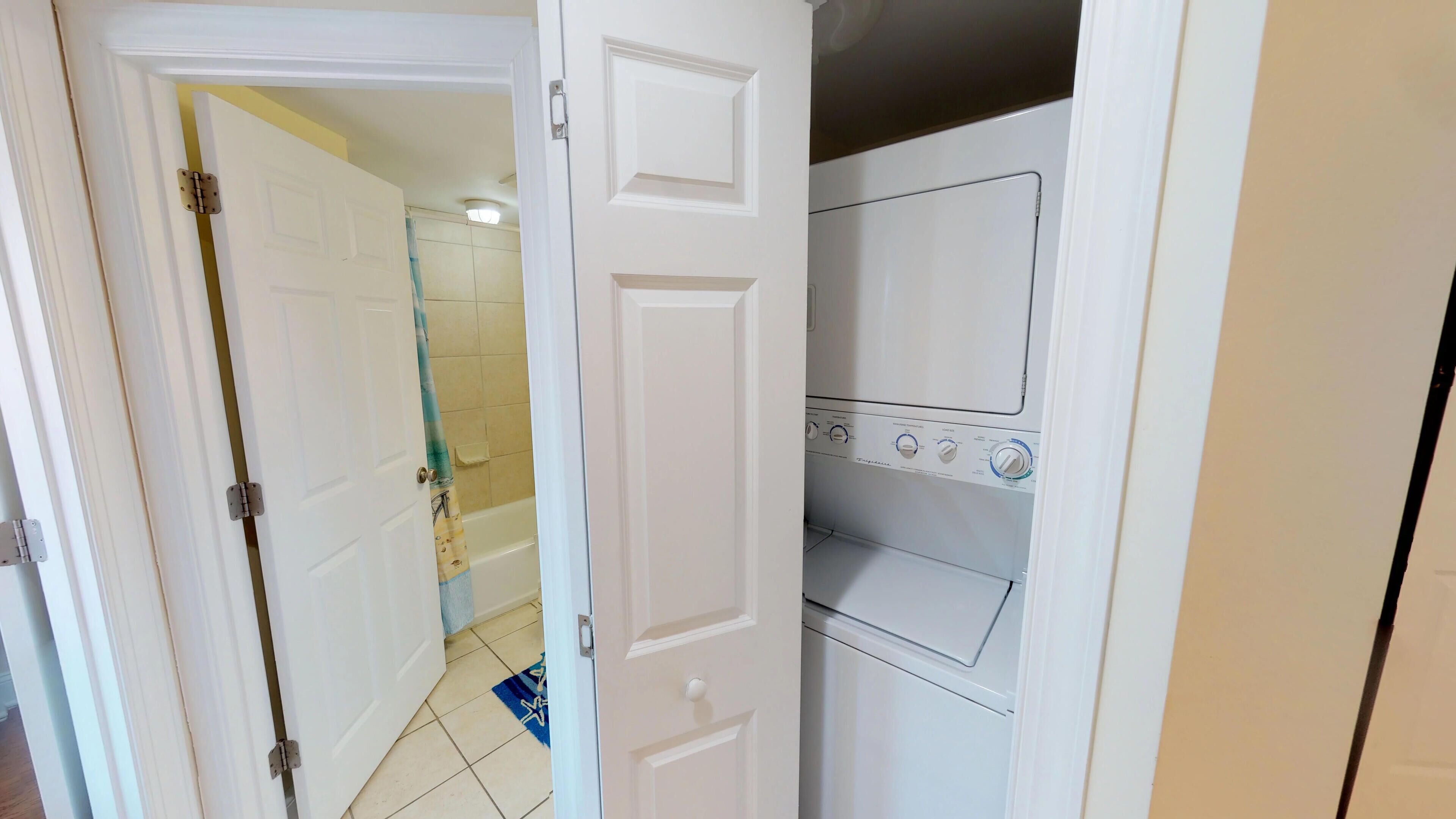 Un cuarto de lavandería con lavadora y secadora, piso de baldosas y una puerta que da a un baño con ducha.