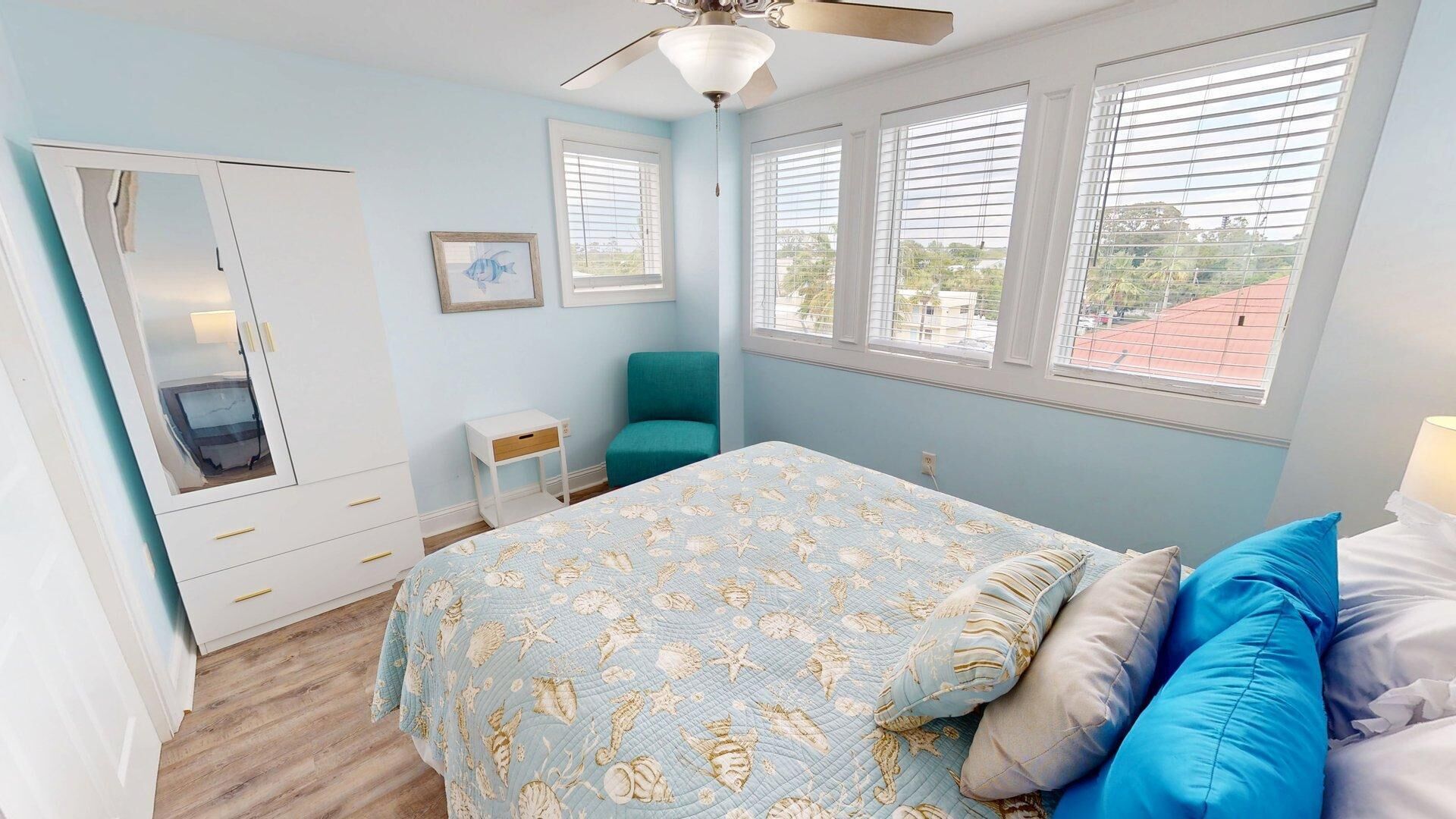 Une chambre à coucher comprenant un lit, un bureau, une chaise, une armoire et un ventilateur de plafond.