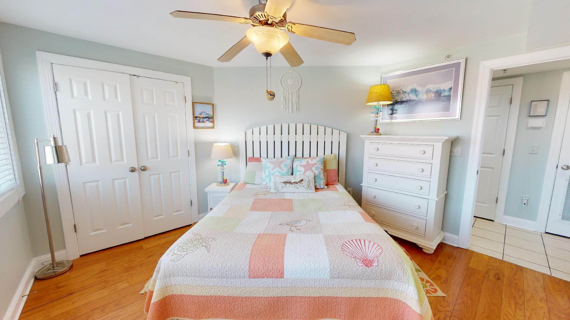 Une chambre à coucher comprenant un lit, une commode, un ventilateur de plafond et une lampe fixée au mur.