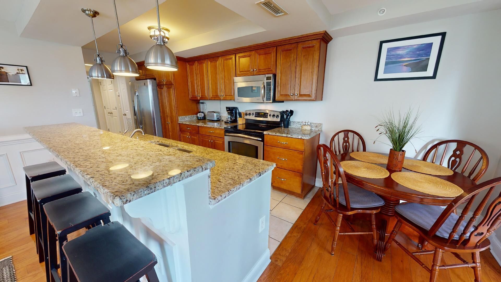A modern kitchen with granite countertops, stainless steel appliances, wooden cabinets, and a dining area with a wooden table and chairs.