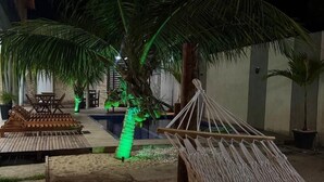 Un hamac sous un palmier, une terrasse en bois et une petite table avec des chaises.