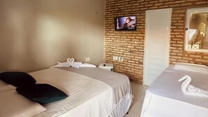 Une chambre d’hôtel avec deux lits, un téléviseur fixé au mur en briques et un miroir.