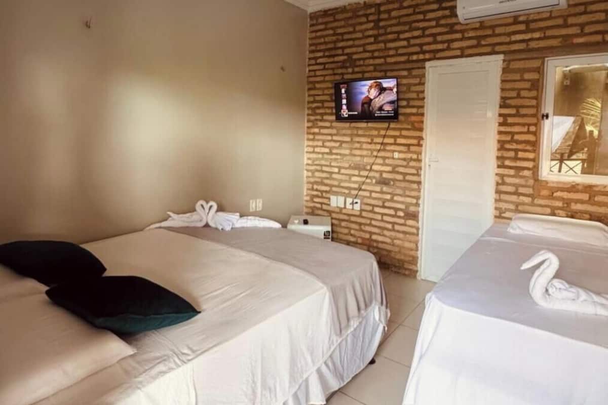 Habitación de hotel con dos camas, un televisor montado en la pared de ladrillo y un espejo.