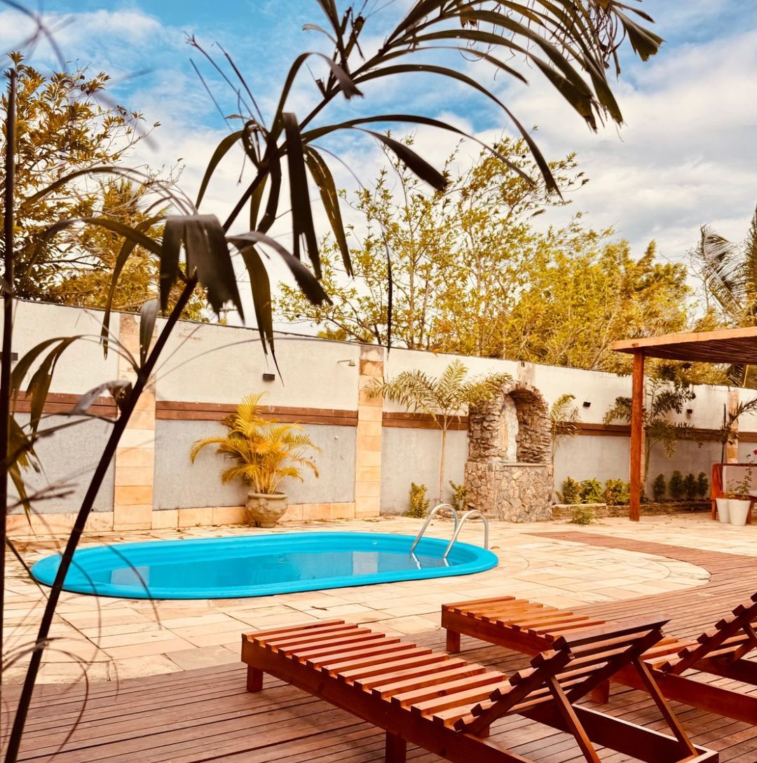 Um deck de madeira com espreguiçadeiras, piscina e um muro de pedra com plantas.